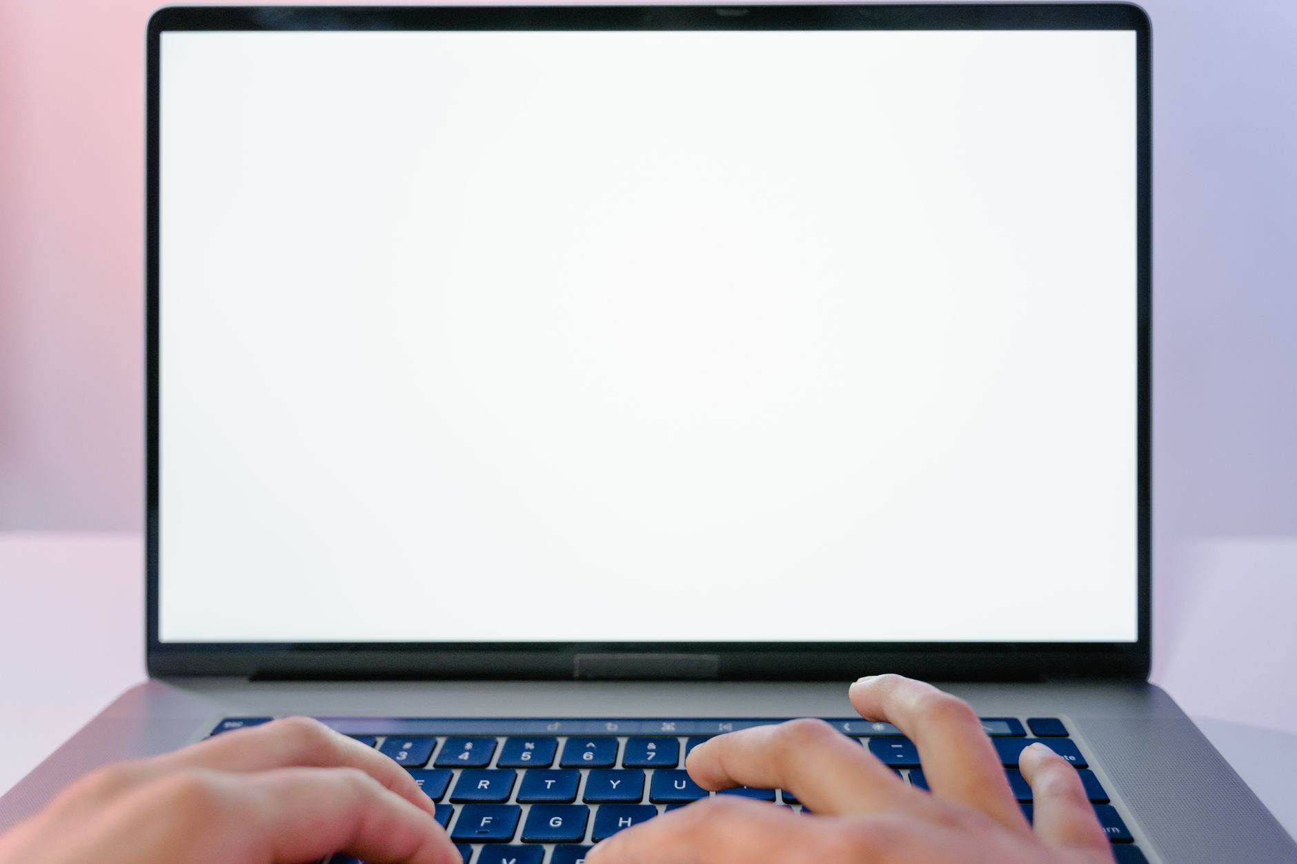 Deux mains tapent sur le clavier d’un ordinateur portable dont l’écran est blanc et vide.