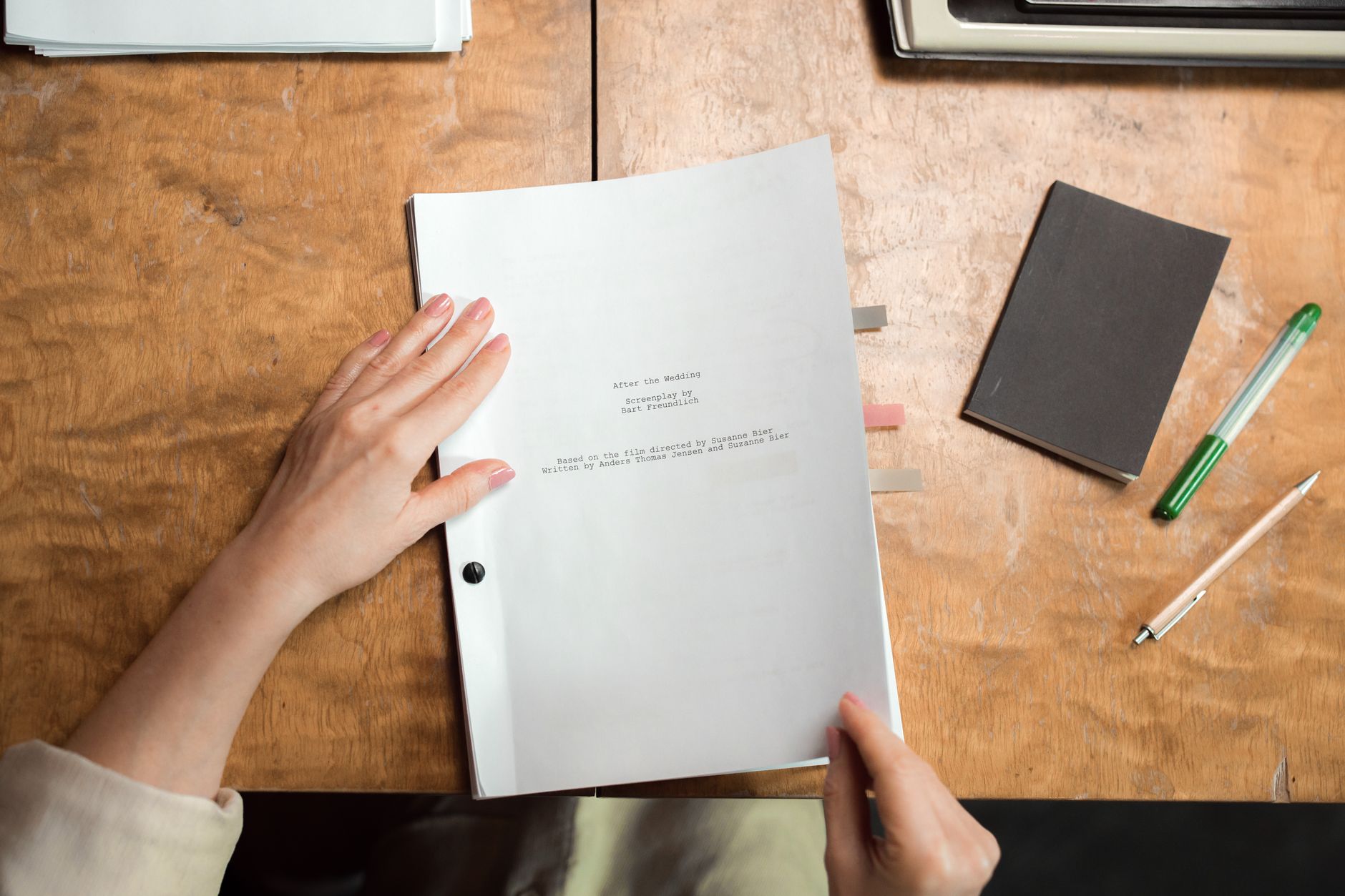 Mains feuilletant un manuscrit relié posé sur un bureau en bois.