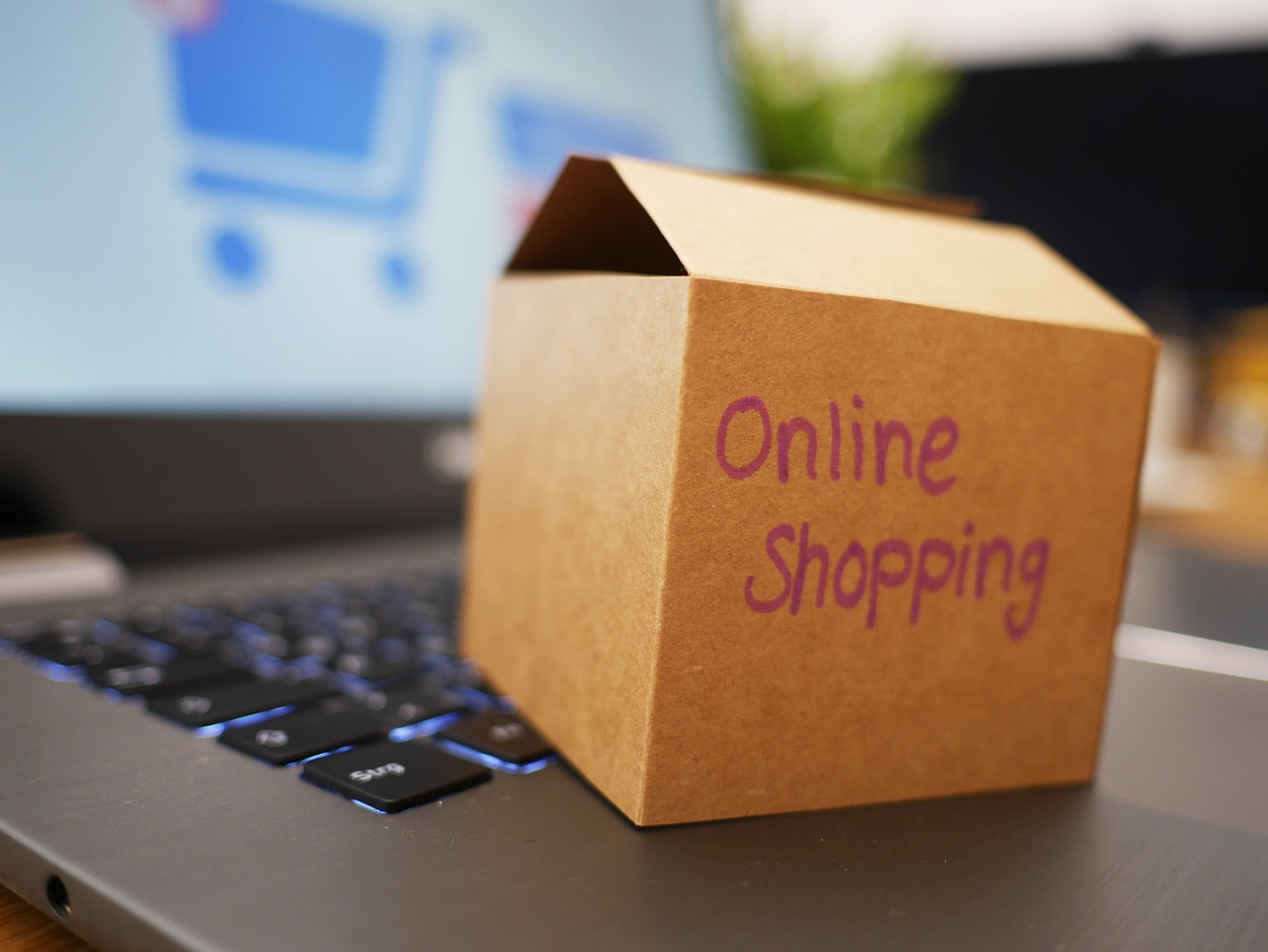 Un petit carton marqué Online Shopping posé sur le clavier d’un ordinateur portable, un panier d’achat flou à l’écran
