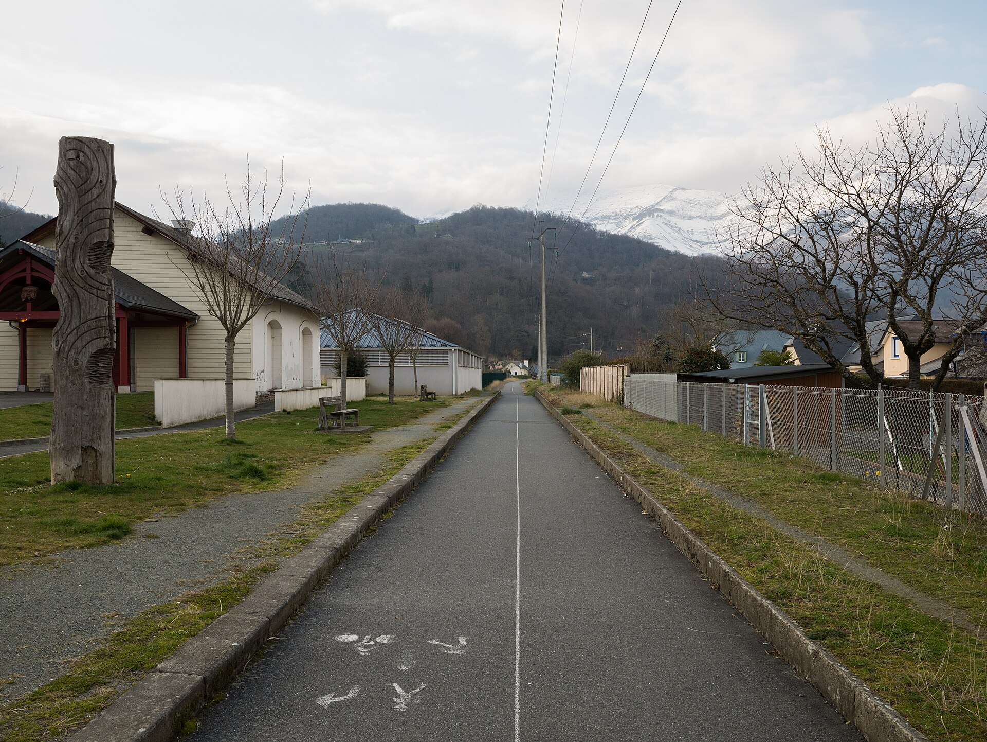 Une voie verte asphaltée qui file entre des maisons vers les montagnes, sans personne