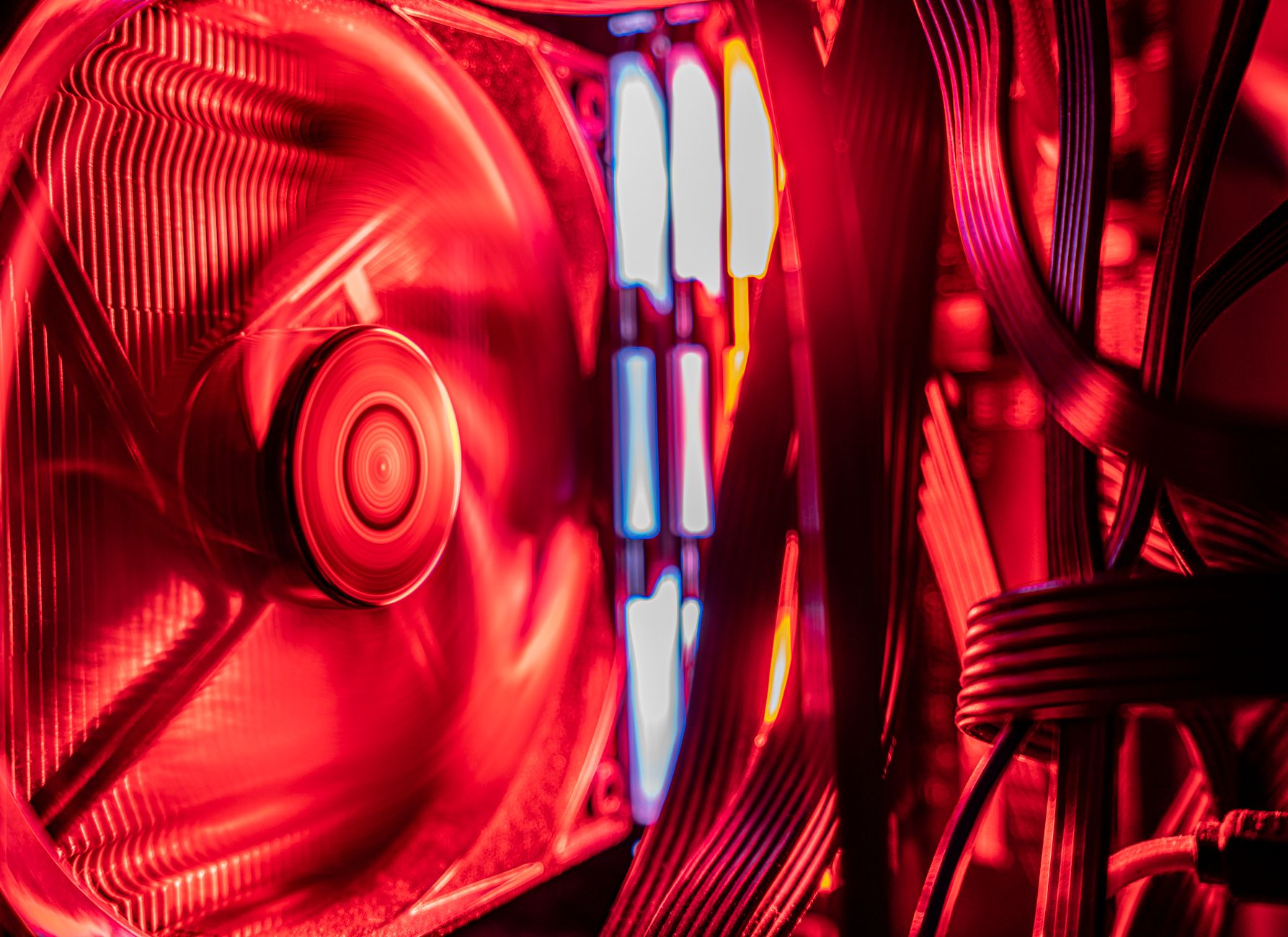 Ventilateur de refroidissement en rotation dans un ordinateur éclairé en rouge, avec des câbles et des modules lumineux.